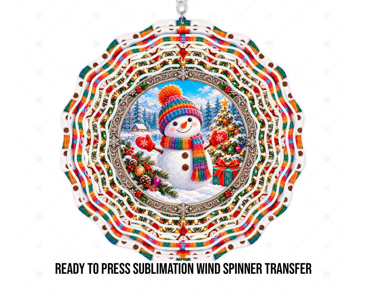 Wind spinner mockup showing snowman artwork for a physical printed sublimation transfer. A smiling snowman in a rainbow knit hat and scarf wears red snowflake mittens beside a decorated Christmas tree and gift. Snowy evergreens, mountains, and a cabin sit behind an ornate silver-toned frame, with rainbow stripes and holiday motifs across concentric scalloped rings.