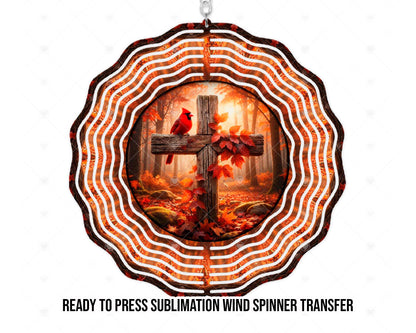 Mockup of a wind spinner sublimation transfer design featuring a red cardinal perched on a rustic wooden cross entwined with red and orange leaves. A sunlit autumn forest, fallen leaves, and mossy rocks fill the background. Concentric scalloped rings carry the warm woodland colors around the central artwork.